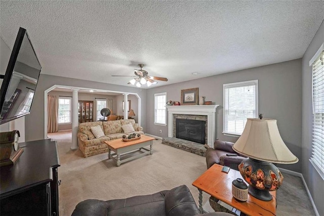 living room featuring a fireplace, a textured ceiling, light carpet, ceiling fan, and decorative columns