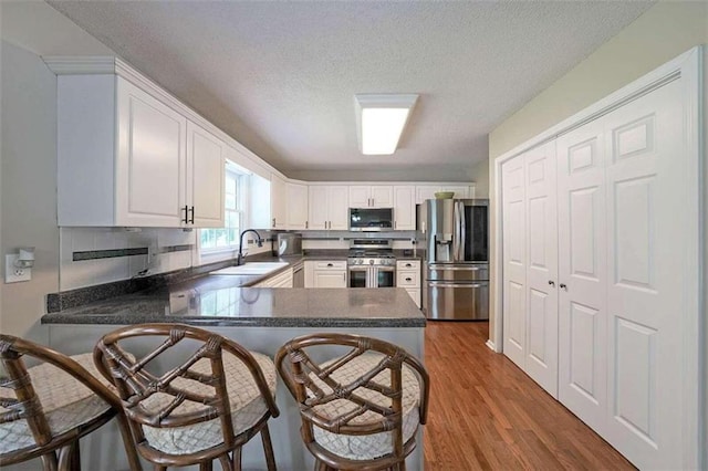 kitchen featuring appliances with stainless steel finishes, hardwood / wood-style floors, sink, kitchen peninsula, and a breakfast bar area