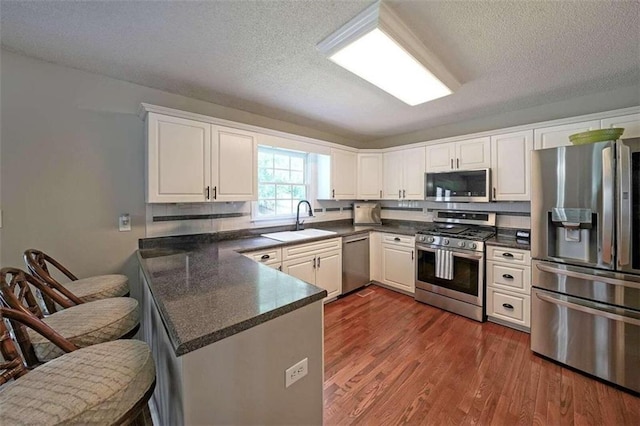 kitchen with kitchen peninsula, stainless steel appliances, dark hardwood / wood-style flooring, and sink