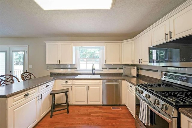 kitchen with hardwood / wood-style flooring, white cabinets, a kitchen bar, sink, and stainless steel appliances