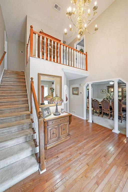 staircase with hardwood / wood-style floors, an inviting chandelier, a high ceiling, and ornate columns