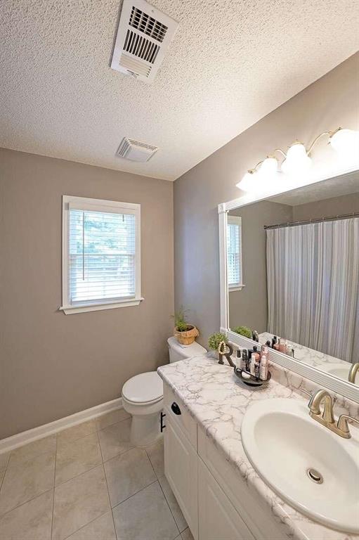 bathroom with tile patterned flooring, a textured ceiling, vanity, and toilet