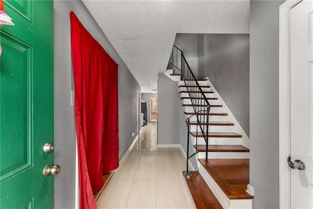 entryway featuring light tile patterned floors, baseboards, stairway, and a textured ceiling