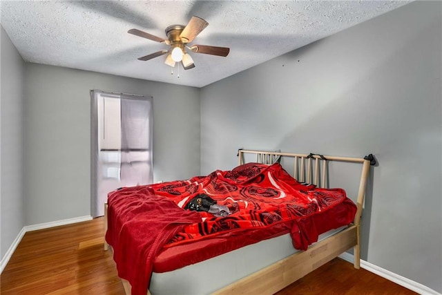 bedroom featuring ceiling fan, a textured ceiling, baseboards, and wood finished floors