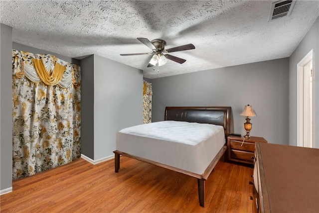 bedroom featuring a textured ceiling, wood finished floors, visible vents, baseboards, and a ceiling fan