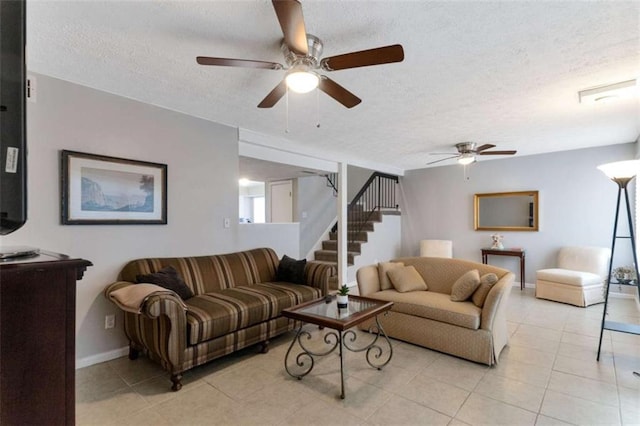 living room with stairway, light tile patterned floors, baseboards, ceiling fan, and a textured ceiling