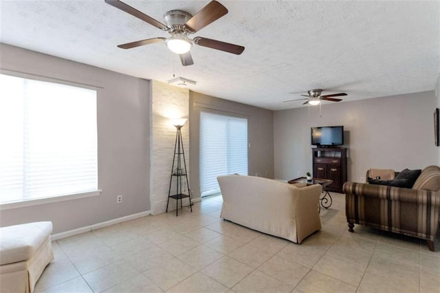 living area with light tile patterned floors, a ceiling fan, baseboards, and a textured ceiling