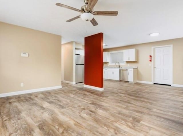 unfurnished living room with light wood-type flooring, a sink, baseboards, and a ceiling fan