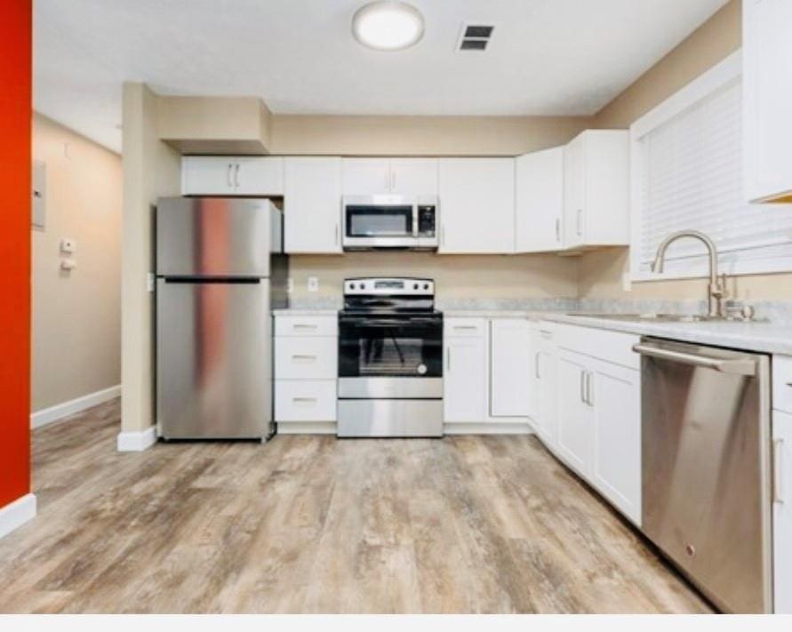 kitchen with a sink, visible vents, light countertops, appliances with stainless steel finishes, and light wood finished floors