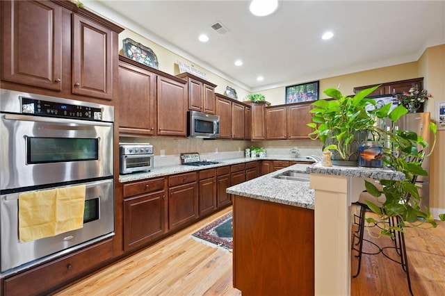 kitchen with appliances with stainless steel finishes, tasteful backsplash, a breakfast bar area, light hardwood / wood-style flooring, and sink