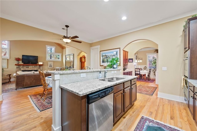 kitchen featuring ceiling fan, a fireplace, an island with sink, light hardwood / wood-style flooring, and dishwasher