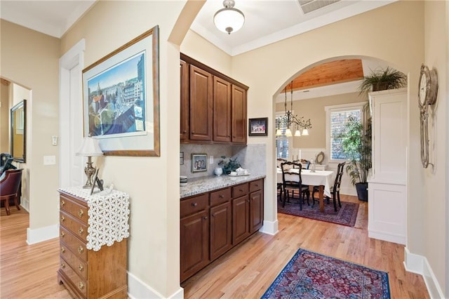 kitchen with tasteful backsplash, dark brown cabinets, hanging light fixtures, light wood-type flooring, and light stone counters