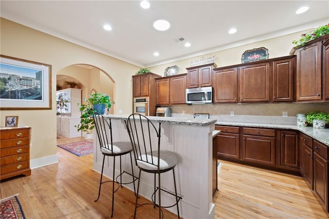 kitchen with a kitchen breakfast bar, backsplash, stainless steel appliances, light stone countertops, and light wood-type flooring