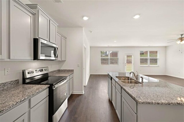 kitchen with appliances with stainless steel finishes, sink, dark hardwood / wood-style flooring, a kitchen island with sink, and light stone countertops