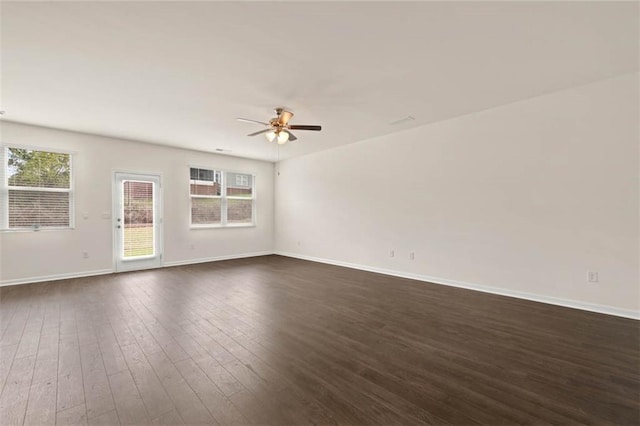 spare room featuring dark wood-style floors, baseboards, a ceiling fan, and a healthy amount of sunlight