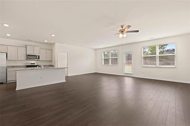 unfurnished living room with a healthy amount of sunlight, dark wood-style floors, ceiling fan, and baseboards