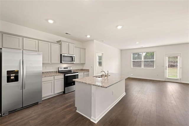 kitchen with appliances with stainless steel finishes, dark wood-style flooring, a kitchen island with sink, and a sink