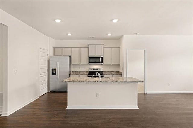 kitchen featuring an island with sink, light stone counters, dark wood-type flooring, stainless steel appliances, and a sink