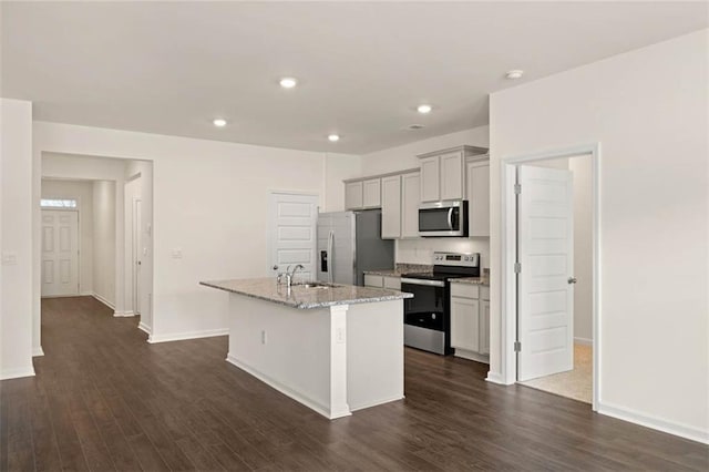 kitchen featuring dark wood-style floors, gray cabinetry, appliances with stainless steel finishes, a sink, and an island with sink