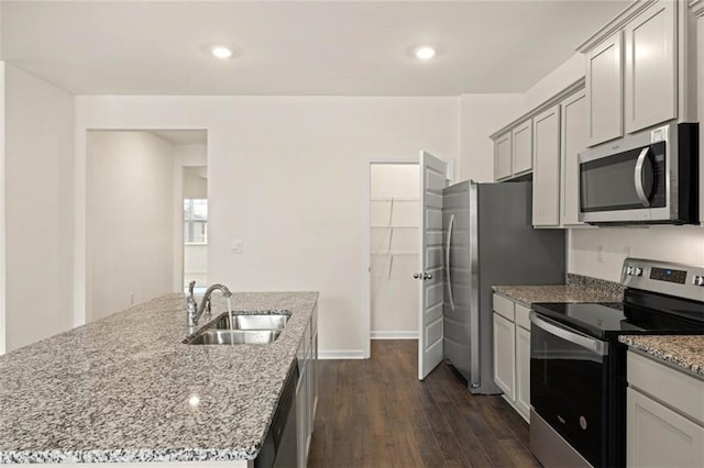 kitchen featuring appliances with stainless steel finishes, dark wood-type flooring, light stone countertops, a kitchen island with sink, and a sink