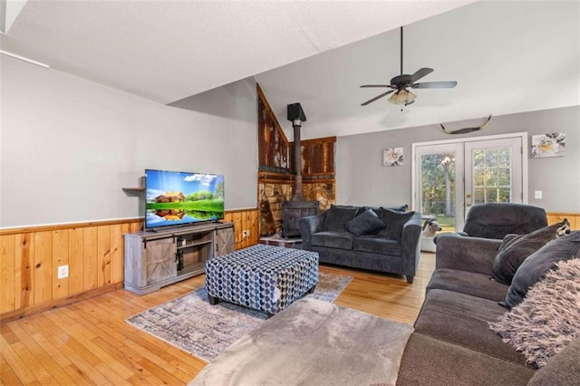 living room with a wood stove, ceiling fan, light hardwood / wood-style floors, vaulted ceiling, and wooden walls