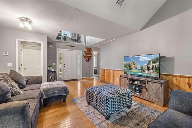 living room with light hardwood / wood-style floors, vaulted ceiling, and wooden walls