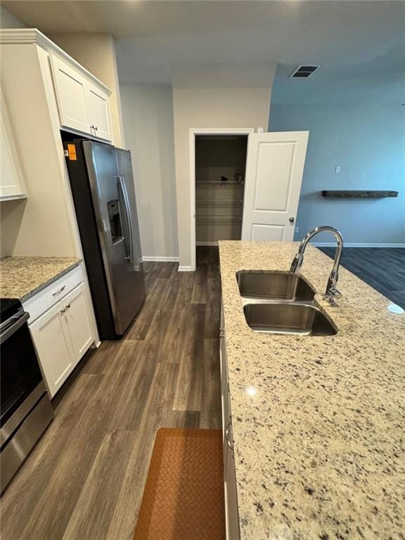 kitchen with dark wood finished floors, light stone counters, stainless steel appliances, white cabinetry, and a sink