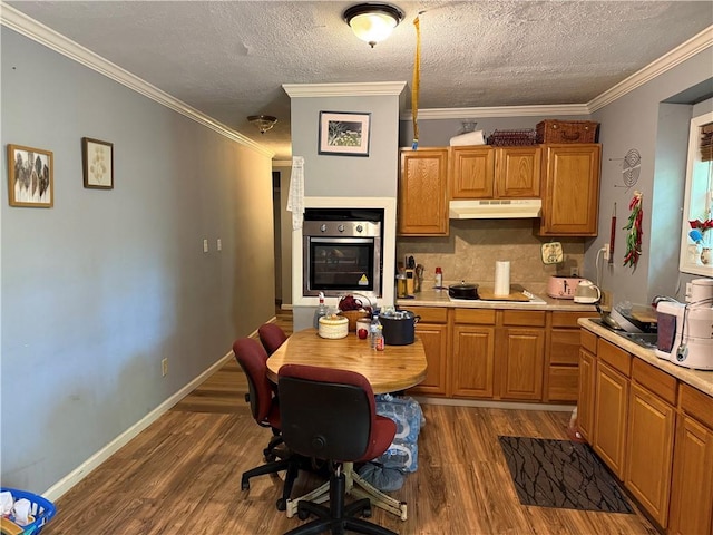 703 Jack Sharp Rd, Colbert, GA 30628 - kitchen featuring stainless steel oven, under cabinet range hood, dark wood-style floors, light countertops, and ornamental molding