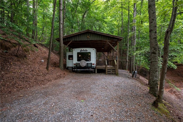 view of car parking with driveway, a forest view, and a carport