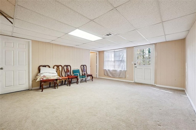 sitting room with wooden walls, baseboards, visible vents, a drop ceiling, and carpet