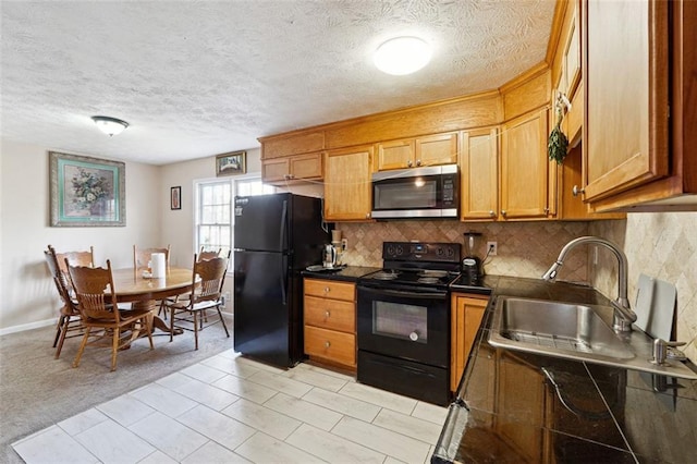 kitchen featuring tasteful backsplash, dark countertops, brown cabinets, black appliances, and a sink