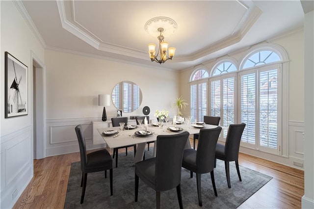 dining space featuring a chandelier, wainscoting, a raised ceiling, and wood finished floors