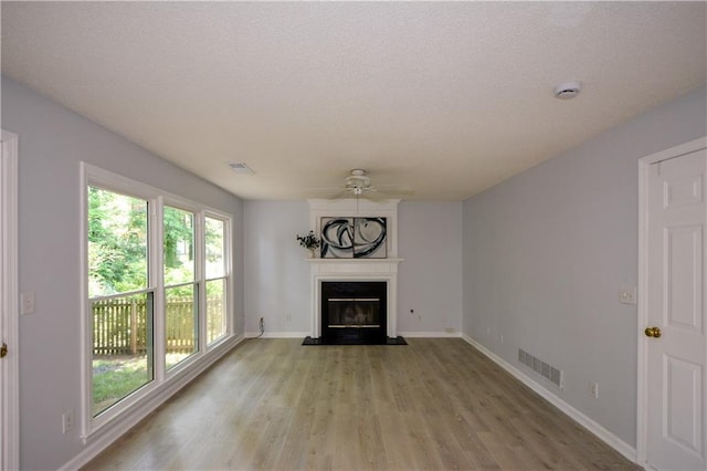 9050 Brockham Way, Alpharetta, GA 30022 - unfurnished living room with a ceiling fan, a glass covered fireplace, light wood-type flooring, baseboards, and a textured ceiling