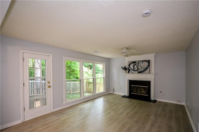 9050 Brockham Way, Alpharetta, GA 30022 - unfurnished living room featuring a glass covered fireplace, ceiling fan, wood finished floors, plenty of natural light, and a textured ceiling
