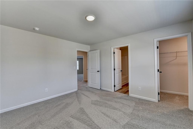 unfurnished bedroom featuring light colored carpet, a spacious closet, connected bathroom, and a closet