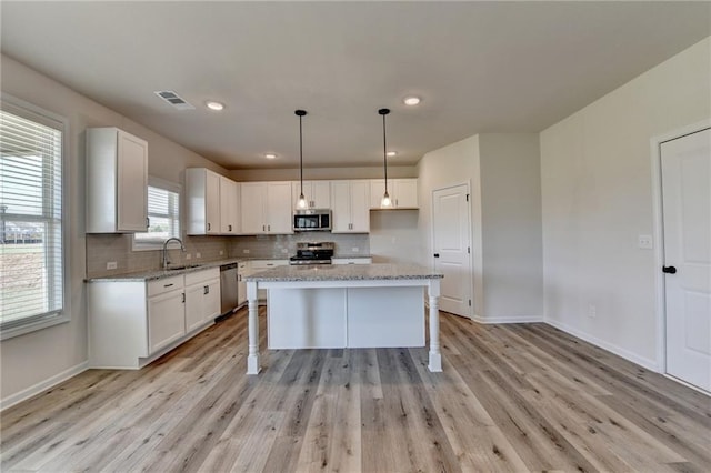 kitchen featuring sink, appliances with stainless steel finishes, a kitchen island, light stone counters, and white cabinetry