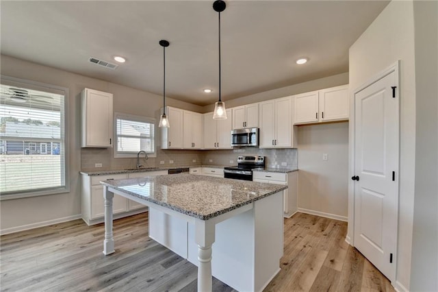 kitchen featuring a center island, white cabinets, sink, appliances with stainless steel finishes, and light stone counters