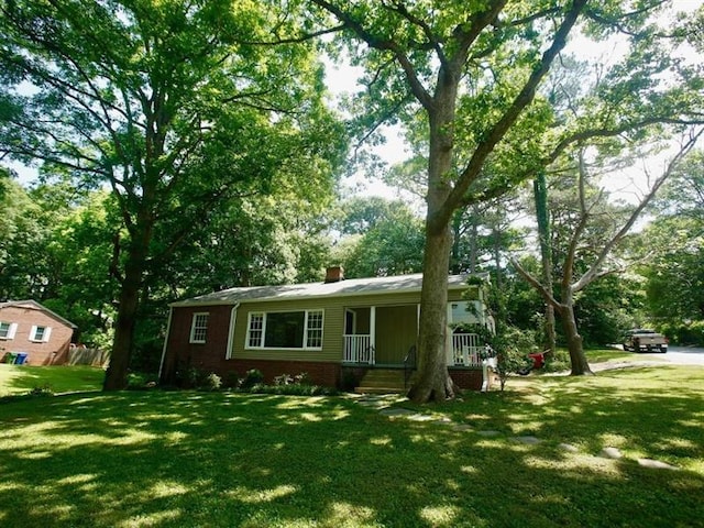 single story home with a front lawn, a chimney, a porch, and brick siding