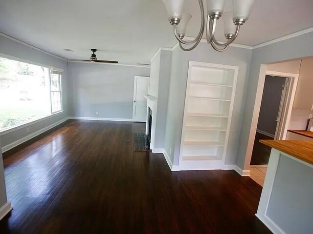 unfurnished living room with built in features, dark wood-style flooring, crown molding, a fireplace with flush hearth, and baseboards