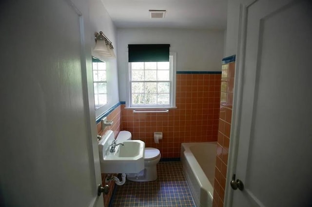 bathroom featuring visible vents, toilet, a bath, tile patterned flooring, and tile walls