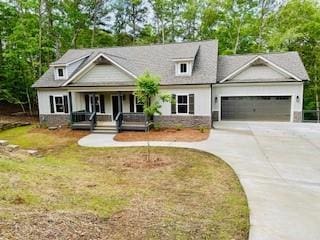 view of front of property with covered porch, concrete driveway, an attached garage, and view of scattered trees