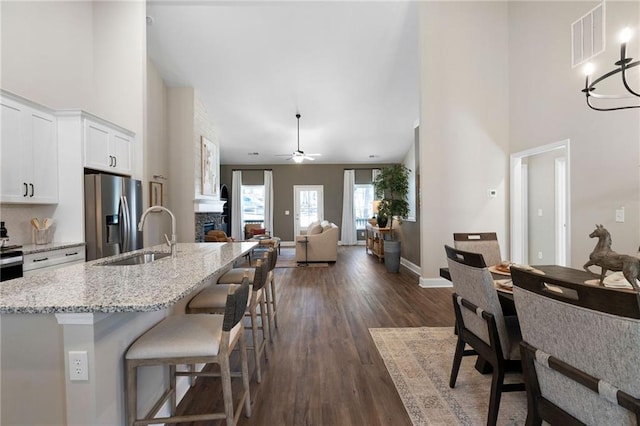 kitchen featuring stainless steel fridge with ice dispenser, a sink, dark wood-style flooring, white cabinetry, and light stone counters