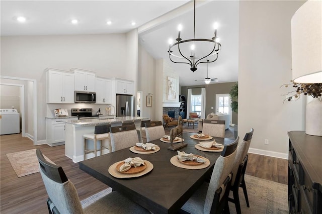 dining room featuring washer / clothes dryer, baseboards, high vaulted ceiling, a chandelier, and wood finished floors