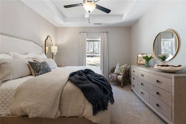 bedroom featuring a raised ceiling, light colored carpet, and a ceiling fan