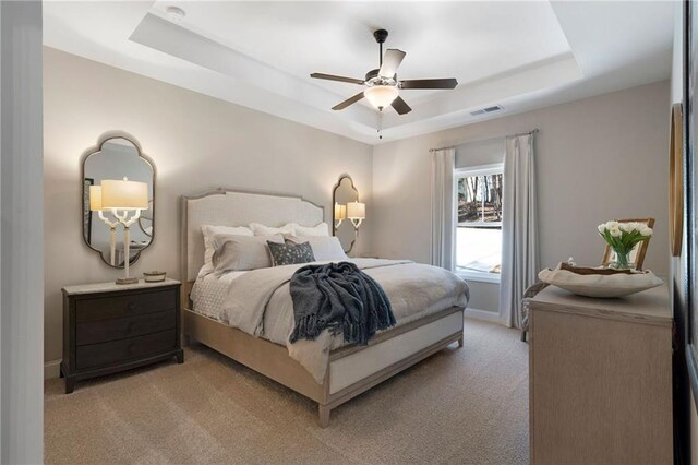 bedroom featuring a tray ceiling, light carpet, ceiling fan, and baseboards