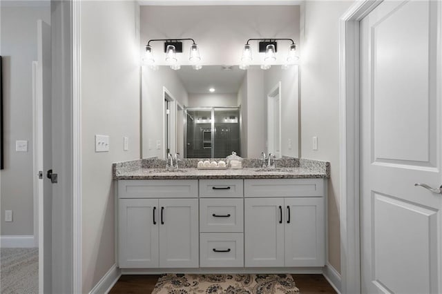 full bathroom featuring a shower stall, double vanity, baseboards, and wood finished floors