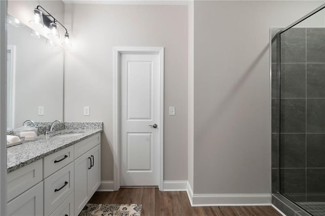 bathroom featuring wood finished floors, a stall shower, double vanity, and baseboards