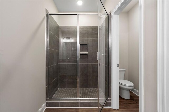 full bath featuring a stall shower, wood finished floors, toilet, and baseboards