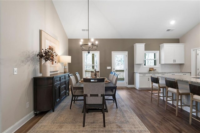 dining space featuring dark wood-style flooring, plenty of natural light, a chandelier, vaulted ceiling, and baseboards