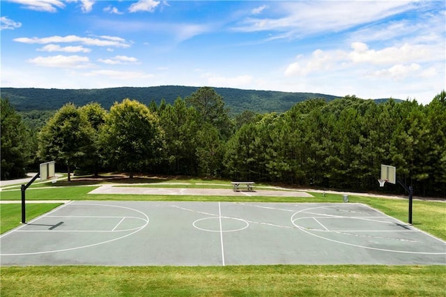view of sport court featuring community basketball court, a wooded view, and a lawn